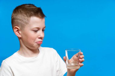 Boş kadehle içeri bakan üzgün genç bir çocuk. Adam mavi arka planda üzgün görünüyor..