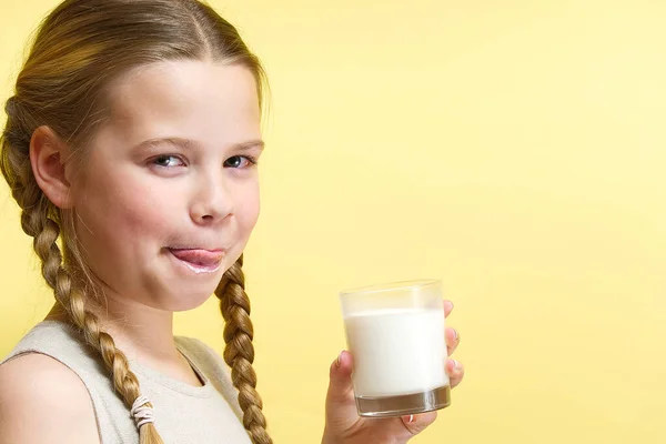 Mädchen mit Zöpfen und Milchbart trinkt Milch auf gelbem Hintergrund. — Stockfoto