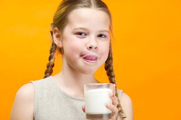 Menina com tranças e leite bigode bebe leite no fundo laranja . — Fotografia de Stock