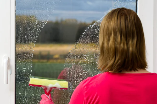 Ελκυστική σύζυγος πλένει ένα παράθυρο. Γάντι χέρι καθαρισμού κουρέλι παράθυρο και σπρέι. Καθάρισμα παραθύρων. έννοια της υπηρεσίας καθαρισμού. — Φωτογραφία Αρχείου