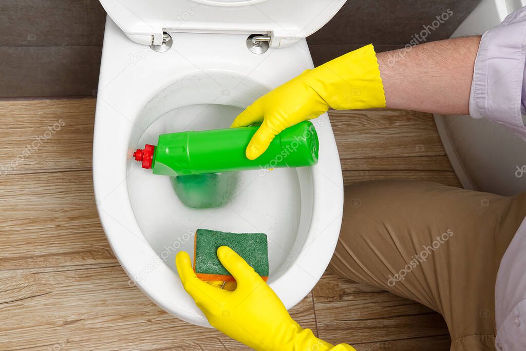 Man disinfecting the toilet seat by spraying a green sanitizer from a bottle. A man disinfects a toilet at home.