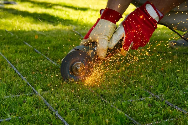 Cutting metal net with grinder on green grass. Sparks from contact materials. Worker outside, cut the steel net. Process with angle grinder.