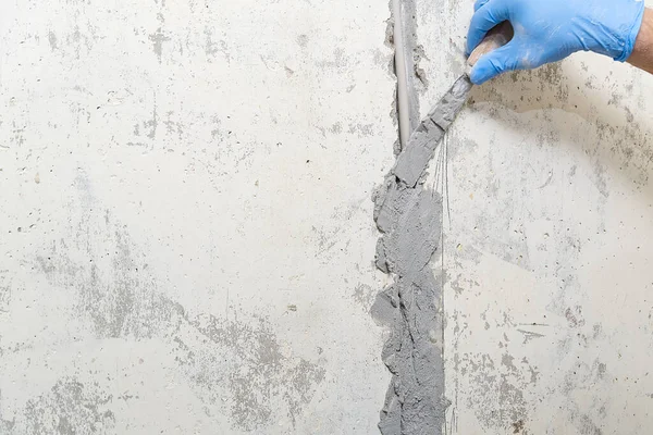 hidden installation of electrical wires for sockets to a concrete wall. The master is plastering the strobes with the wire before the molar works. repair in an old apartment and transfer of sockets.