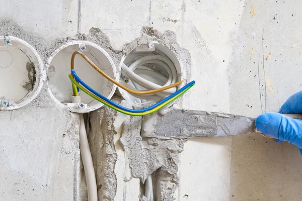 Скрытая установка электрических проводов для розетки к бетонной стене. Хозяин оштукатурирует стробы проволокой до того, как зуб заработает. ремонт в старой квартире и перенос розетки . — стоковое фото