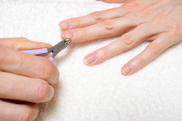 Vrouwen hand verwijderen nagel nagelriemen op licht witte tafel. Zorg voor droge, overgroeide nagelriemen. Sluitingsdatum. — Stockfoto