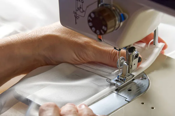 A woman works on a sewing machine. seamstress sews white curtains, close up view. — Stock Photo, Image