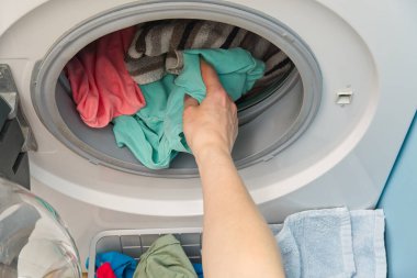 Kadın eli çamaşır makinesinden çamaşırları çıkarır. Kadın çamaşır makinesine çamaşır koyar..