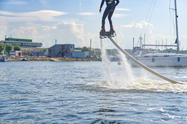 Flyboard 'da eğlenen bir adam. Limandaki nehirde güneşli bir yaz gününde uçağa binmek. Ekstrtrik su aktivitesi uçuş panosu.