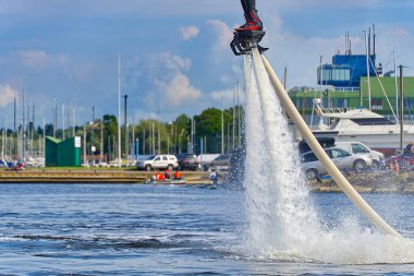 Flyboard 'da eğlenen bir adam. Limandaki nehirde güneşli bir yaz gününde uçağa binmek. Ekstrtrik su aktivitesi uçuş panosu.