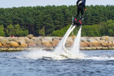 Flyboard 'da eğlenen bir adam. Limandaki nehirde güneşli bir yaz gününde uçağa binmek. Ekstrtrik su aktivitesi uçuş panosu.
