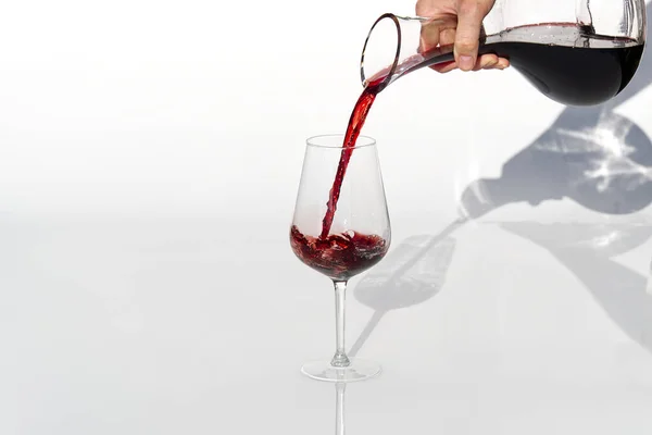 Sommelier nalévá červené víno z karafy na víno na bílém pozadí. — Stock fotografie