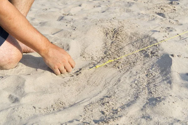 Un piolo di metallo spinto nella sabbia per tirare la corda fuori dalla tenda. Campeggio su una spiaggia di sabbia. uomo alza una tenda sulla spiaggia. concetto di viaggio natura. — Foto Stock