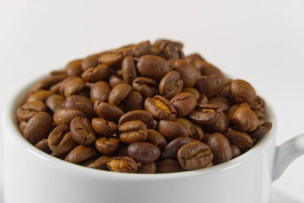 Granos de café en taza blanca, primer plano. Taza de café blanco con semillas de café sobre fondo blanco. Concepto Para el Día Internacional del Café. — Foto de Stock