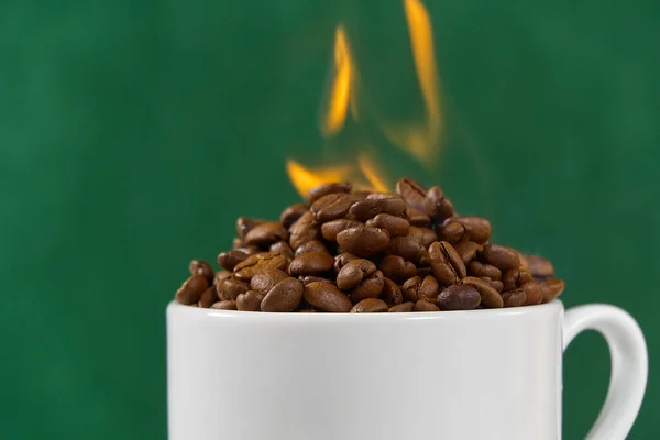 International day of coffee concept. close-up white coffee cup full of coffee beans on green background with fire on top.