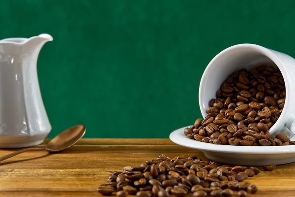 International day of coffee concept. close-up white coffee cup full of coffee beans on dark green background.