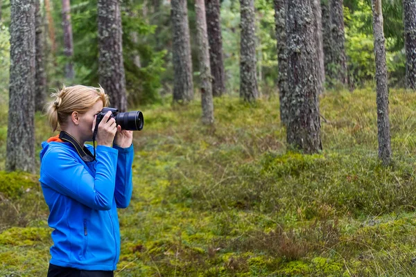 Giovane donna trekking tra gli alberi e scattare foto con macchina fotografica. fotografa donna di mezza età scattare foto nella foresta autunnale. Natura fotografia. — Foto Stock