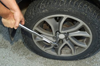 Tekerlek değiştiren adam. Lastik değiştirici patlak araba lastiğini değiştiriyor. Tamirci elleri, kriko üzerinde yükseltilmiş bir arabanın lastiğini söker Yolda ya da lastik yardım kavramında yardım eder.