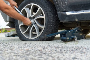 Tekerlek değiştiren adam. Lastik değiştirici patlak araba lastiğini değiştiriyor. Tamirci elleri, kriko üzerinde yükseltilmiş bir arabanın lastiğini söker Yolda ya da lastik yardım kavramında yardım eder.