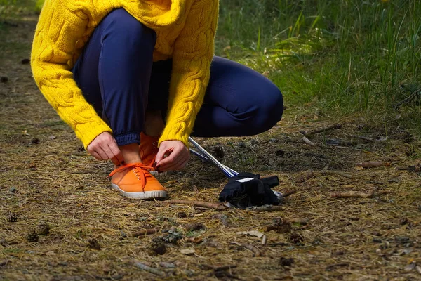 Sporty hiking woman tying shoelaces on her jogging shoes while taking a break after hiking in autumn forest. hiking concept, healthy outdoor lifestyle.