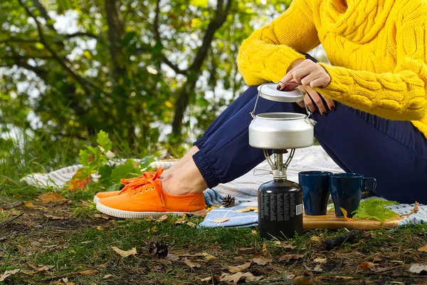 young beautiful girl in a yellow sweater makes coffee in the forest on a gas burner. Making coffee on a primus stove in the autumn forest, step by step. Camping in autumn forest concept