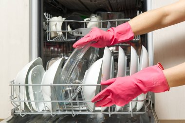 Açık entegre bulaşık makinesinde kirli tabak. Ev hanımının eli bulaşık makinesine kirli bulaşıkları koyuyor. Yıkanmadan önce kirli bulaşıklarla birlikte bulaşık makinesini aç. Kadınlar eldiven takar, tabakları makineye yerleştirir.