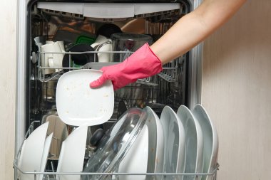 Açık entegre bulaşık makinesinde kirli tabak. Ev hanımının eli bulaşık makinesine kirli bulaşıkları koyuyor. Yıkanmadan önce kirli bulaşıklarla birlikte bulaşık makinesini aç. Kadınlar eldiven takar, tabakları makineye yerleştirir.