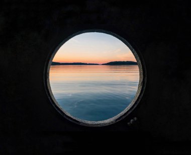 Denizde gün batımı. Güzel bir günün sonu geminin liman deliği ile fotoğraflandı