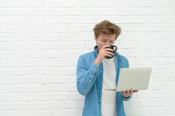 Portrait of young man standing, holding laptop and drink coffee — Stock Photo, Image