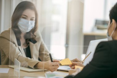 Coronavirus covid-19 salgınını korumak için sosyal mesafeye bölme kullanılarak takılan iki Asyalı iş adamı. Sosyal ve iş mesafesi yeni normal yaşam tarzı.