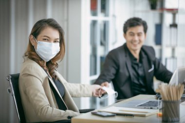 Coronavirus covid-19 salgınını korumak için iş arkadaşıyla yüz maskesini paylaşacak bir iş kadını. Sosyal ve iş mesafesi yeni normal yaşam tarzı.