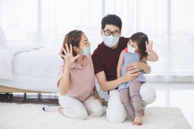 Yüzünde tıbbi maskeler olan Asyalı aile, PM2.5 toz, duman, hava kirliliği ve COVID-19 'u önlemek için oturma odasında dururken kameraya bakıyor. Sağlık hizmetleri kavramı.