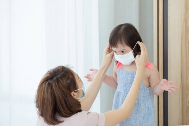 Asyalı bir anne kızının sağlıklı yüz maskesi takarak evde oturuyor. PM2.5 tozu, duman, hava kirliliği ve COVID-19 'u önlemek için. Sağlık hizmetleri kavramı.