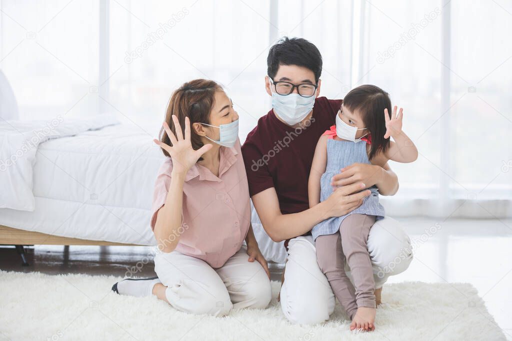 Asian Family in medical masks on the face looks at the camera while standing in the living room at home to prevent PM2.5 dust, smog, air pollution and COVID-19. Healthcare concept.