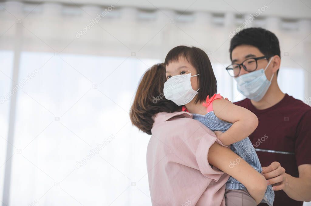 Asian Family in medical masks on the face looks at the camera while standing in the living room at home to prevent PM2.5 dust, smog, air pollution and COVID-19. Healthcare concept.