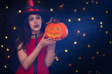 Kırmızı kostüm giymiş güzel bir kız elinde balkabağı olan bir cadı gibi Cadılar Bayramı partisinde korkunç davranıyor..