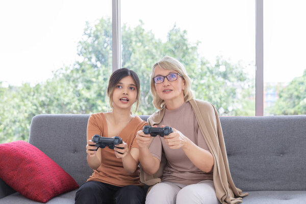 Multicultural family, mom and daughter playing video game on a couch together in the white living room at home.Unusual appearance, diversity, heredity concept.