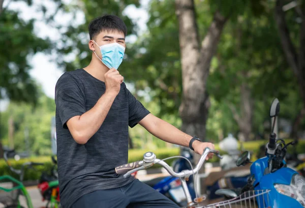 young tall young Asia man with surgical mask and with vintage bike at the car park for reduce infection of coronavirus covid-19 pandemic.New normal lifestyle.