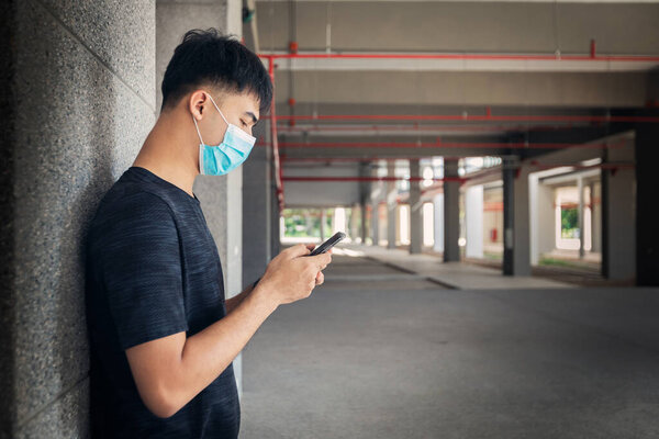 Portrait of young Asian man using smart phone and wearing face mask to protect and prevent from the spread of viruses in the city during COVID-19 pandemic. 