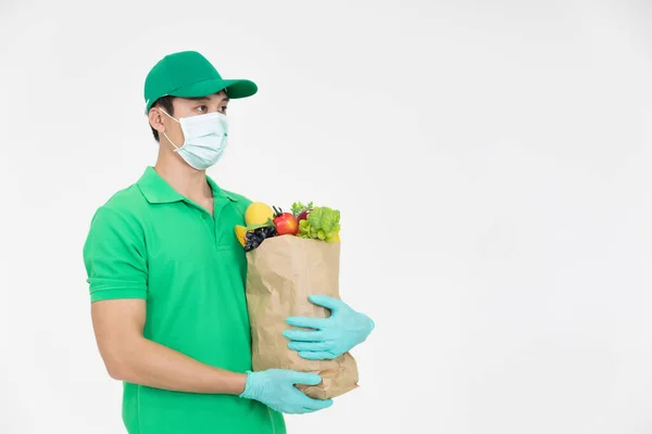 The smart food delivery service man in green uniform wearing face mask handing fresh food to recipient for customer is shopping on line order .Express delivery, food delivery, online shopping concept.