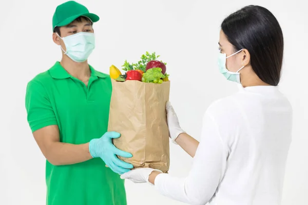 The smart food delivery service man in green uniform wearing face mask handing fresh food to recipient and young woman customer receiving order,express delivery, food delivery, online shopping concept.