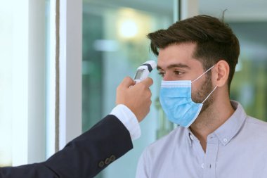 Vücut ısısı kontrolü, resepsiyonist ve konuk otelde konuşurken maske takıyor. Covid 19 ve Coronavirus enfeksiyon koruması ve koruyucu politika konsepti. .