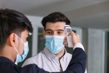 Vücut ısısı kontrolü, resepsiyonist ve konuk otelde konuşurken maske takıyor. Covid 19 ve Coronavirus enfeksiyon koruması ve koruyucu politika konsepti. .