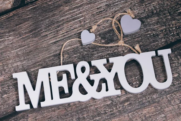 Grey letters me and you with little hearts on wooden background