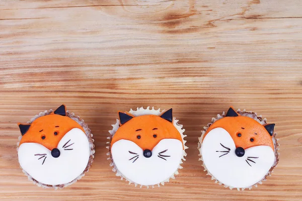 Three decorated cupcakes with fox face from almond paste in detail on wooden background