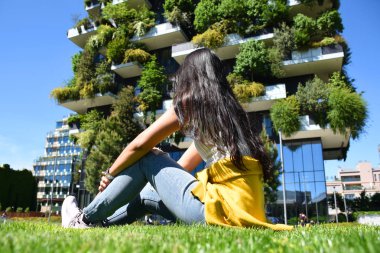 Güzel Tay tabaklanmış esmer Bosco Verticale önünde oturuyor, Dikey Orman konut kuleleri ve dikey bir orman olarak dikilen 900 ağaç arıyor