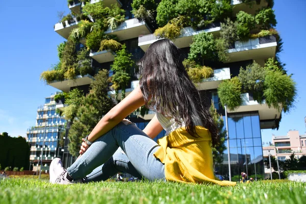 Güzel Tay tabaklanmış esmer Bosco Verticale önünde oturuyor, Dikey Orman konut kuleleri ve dikey bir orman olarak dikilen 900 ağaç arıyor