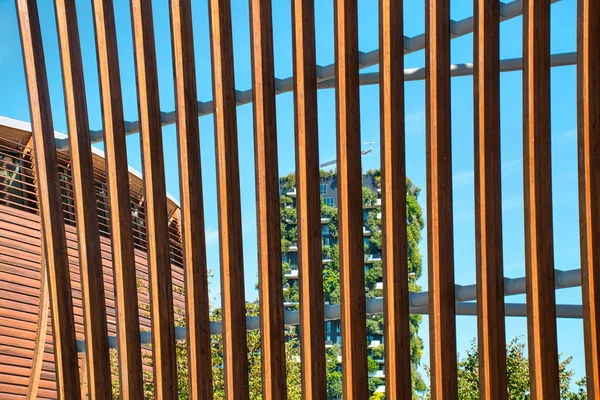 Milan, Italy, 06.29.2020: View through a wooden fence of the Vertical Forest (Bosco Verticale) Innovative Green House Skyscraper representing commitment to sustainable economy designed by Boeri Studio