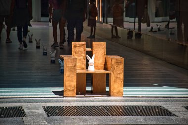 Milan, İtalya 08.16.2020: Milan sokaklarında modern ahşap bir sandalyede oturan beyaz bir tavşan