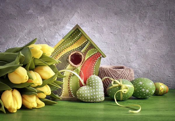 Желтые тюльпаны, птичий домик и крашеные пасхальные яйца с фаршем — стоковое фото