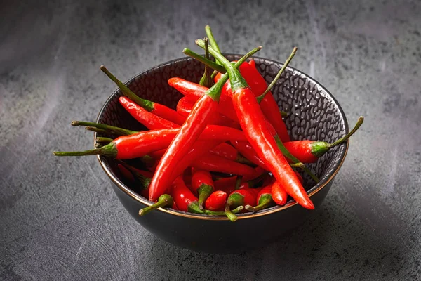 Close-up op rode hete chili pepers in zwarte keramische kom over donker — Stockfoto